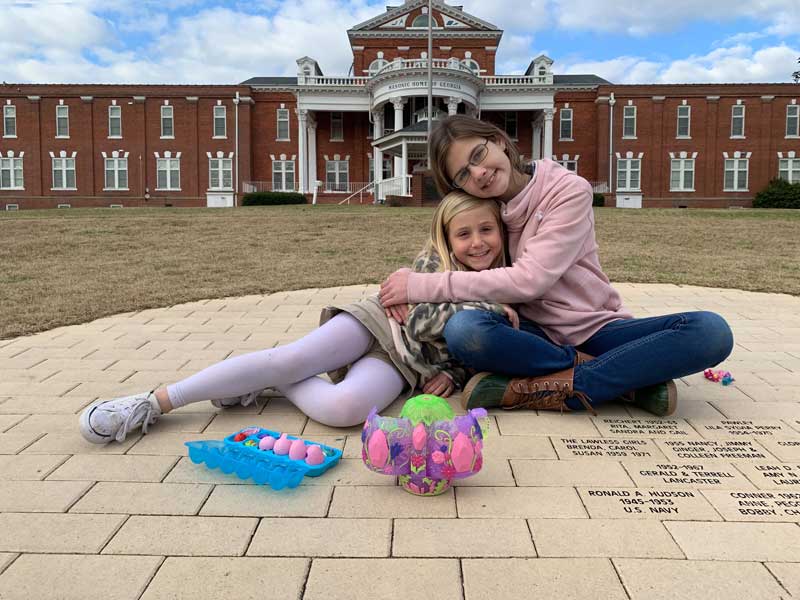 Two residents of the masonic home of georgia smile while sharing a hug in front of our main building.